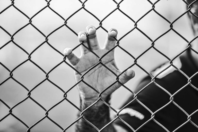 Hand clutching a chain link fence