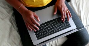 Online community check-ins - a person sitting on a bed with their hands on a laptop.