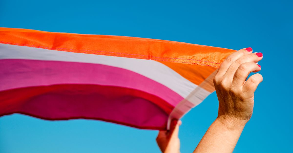 A Lesbian Pride flag held by a white woman's hands, blowing in the wind