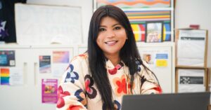 Kyra's, a Malaysian woman sat at her laptop. She is looking directly into the camera